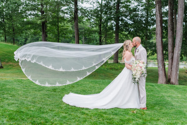 Bride and groom posing on the lawn at The Grandview with the bride's veil flowing