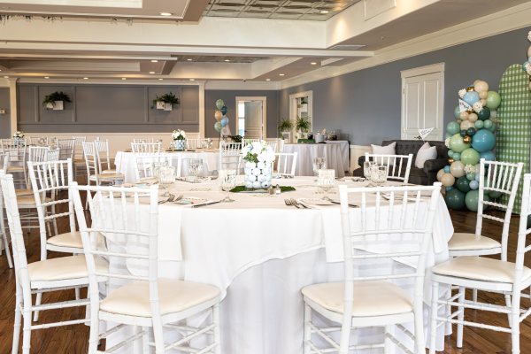 Tables and chairs in the ballroom at The Grandview Venue. The room is decorated with blue, green, and cream colored balloons as well as golf ball centerpieces.