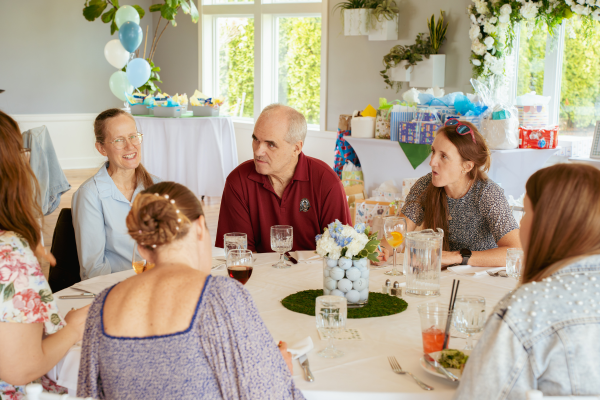 Guests chatting at a baby shower event at The Grandview. Room is decorated with greenery, white flowers, blue and green balloons, and centerpieces made of golf balls and fake grass.