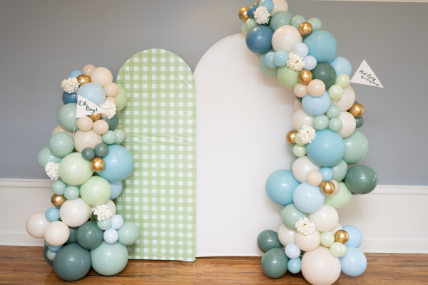 White and gingham green backdrop with cream, green, and blue balloons and white flowers for a baby shower at The Grandview.